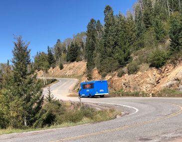 Blue passenger bus driving on a windy mountain road