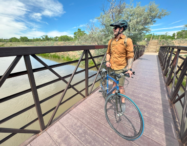 Picture of a man standing next to his bicycle on a bridge over a river in Albuquerque