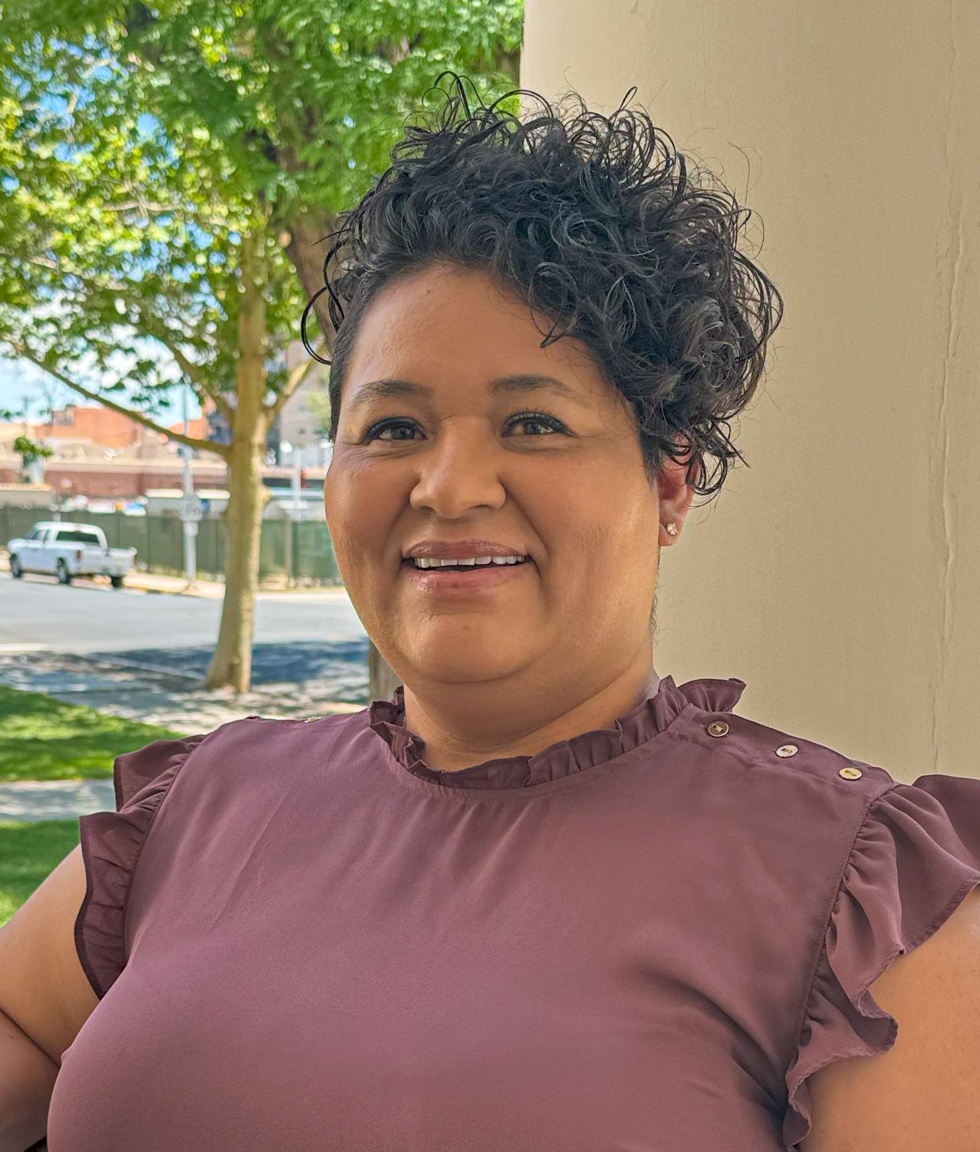Picture of a woman standing outside on a sunny day and smiling at the camera