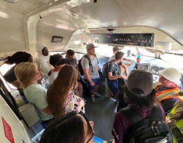 Picture of a group of high school students and a train engineer inside the Rail Runner train