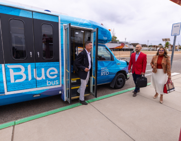 People exiting the NCRTD Blue commuter bus with the Rail Runner train in the background