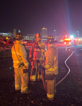 Picture of three firefighters standing outside at night with downtown Albuquerque in the background