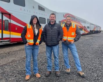 Picture of three people dressed in bright orange safety vests standing in front of the Rail Runner